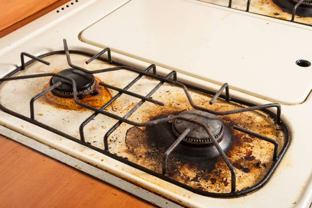 Hands scrubbing stove top with a natural cleaner to remove stubborn burnt grease